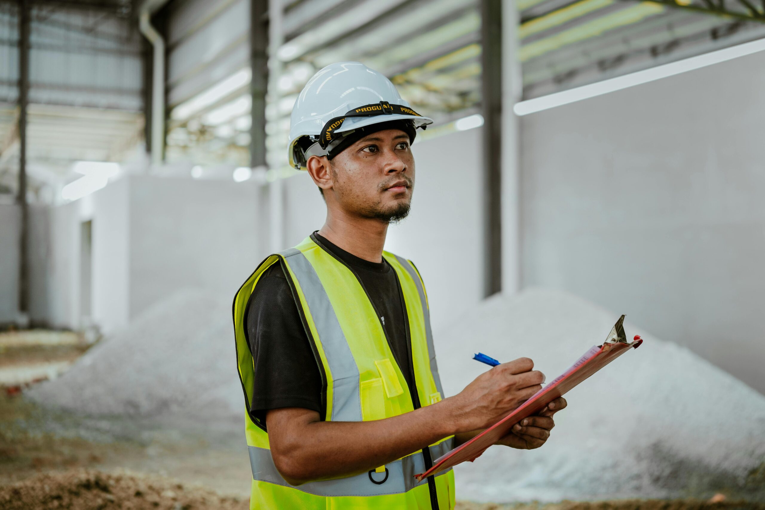 Asian construction worker in a factory setting, using a clipboard for inspection tasks in Banting, Malaysia.